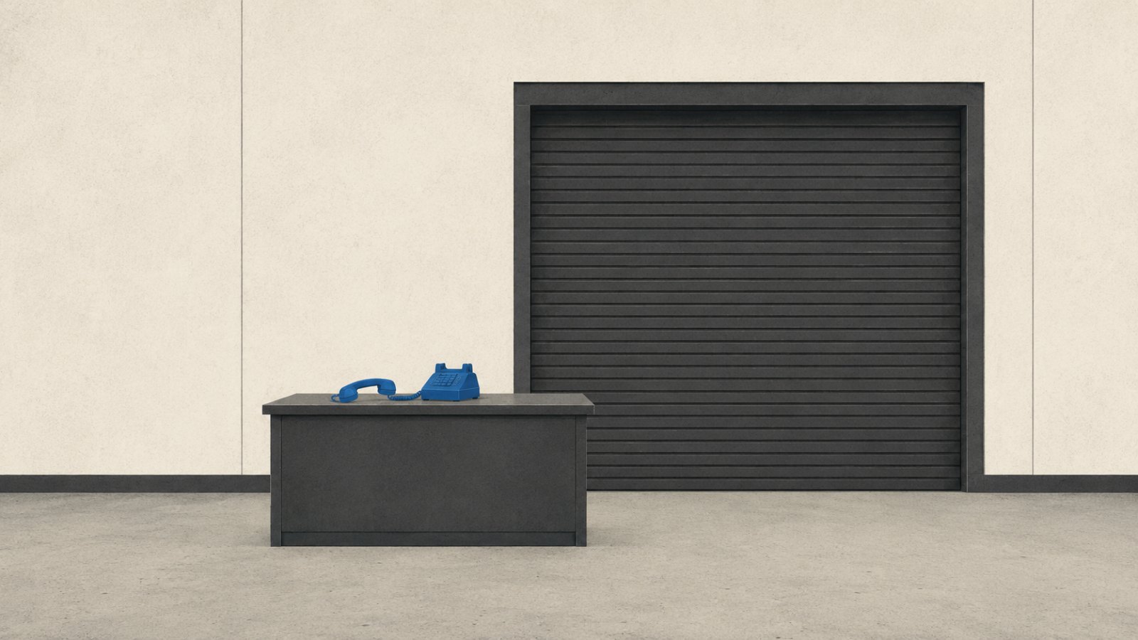 An empty facility office desk with a blue phone off the hook, beside a closed roll-up storage door